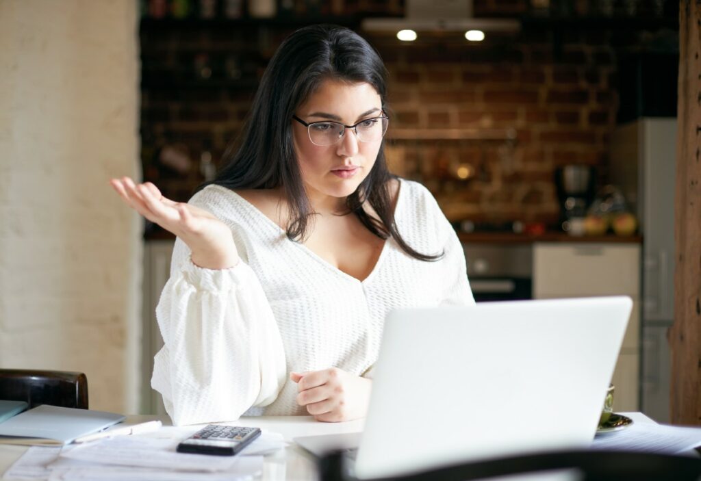 mulher com os cabelos pretos, óculos de grau e camisa branca pensando em qual plataforma de ecomerce irá escolher